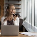 woman with phone to her mouth giving instructions to a voice assistant