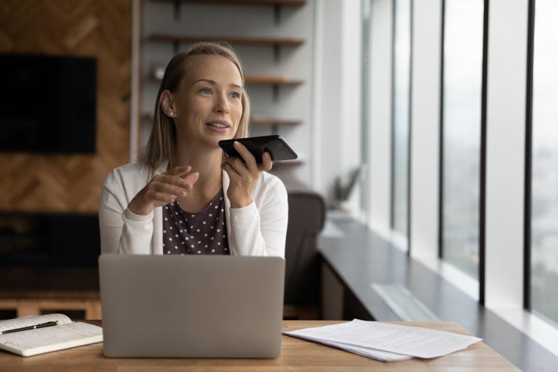 woman with phone to her mouth giving instructions to a voice assistant